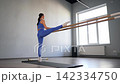 Graceful sporty fit attractive woman practicing barre fitness workout, doing one legged splits stretch, improving flexibility and leg extension while exercising in health club. 142334750