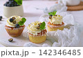 Delicious cupcakes with white frosting blueberries and mint arranged on a textured surface 142346485