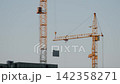 Two large cranes stand tall against the blue sky. They are positioned at a construction site 142358271