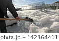 Shoveling Snow Around a Greenhouse: Overcoming Winter Challenges with Manual Labor in a Snow-Covered Landscape and Clear Blue Skies Above 142364411