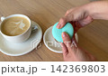 Blue Macaron Broken in Half by Female Hands Beside Cup of Coffee Showing Creamy Filling Inside French Dessert 142369803