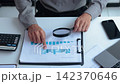 Close-up Businessman Analyzing or Auditing Financial Growth Charts with Magnifying Glass in the office. 142370646