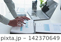 Close-up corporate accountant hand holding pen reviewing revenue growth charts and budget document in bright office. 142370649