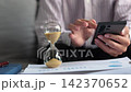 Running hourglass on the table with man using smartphone. Concept for time management or daily active screen time. 142370652