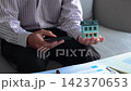Businessman using smartphone and holding miniature home. Concept for real estate online management. 142370653