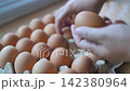 Close-up video of a hand selecting and inspecting brown chicken eggs arranged in a cardboard carton 142380964