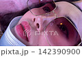 Extreme close-up portrait of young woman wear glasses and face mask while lying and watching phone 142390900
