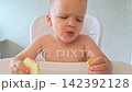 Toddler boy sitting in a high chair and eating a fresh apple slice 142392128