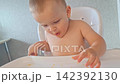 Toddler sitting in a high chair joyfully eating tangerine 142392130