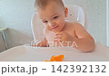 Baby eating mandarin segments in high chair 142392132