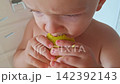 Toddler boy eating a ripe green pear in his high chair 142392143