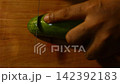 Hand slicing fresh green cucumber on wooden cutting board with kitchen knife 142392183