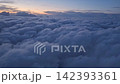 A view from the plane of endless blue clouds stretching into the distance. The sunset glows faintly, painting the sky with soft hues. High in the sky, the clouds float beneath the fading twilight. 142393361