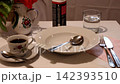 A simulation of an earthquake on a table with a cup of coffee, a glass of water, a plate, cutlery, and a vase of flowers, with everything shaking as if during an earthquake 142393510