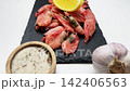 A bowl of spices and a head of garlic lie on a black slate board in front of a handful of shrimps with a slice of lemon on top on a white background, a smooth approach. The concept of seafood 142406563