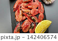 Pink shrimps with lemon slices, spices and garlic lie on a black slate board on a gray background, the camera moves smoothly to the side. The concept of seafood, cooking, seasoning, taste. High 142406574