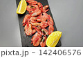 Pink shrimps are lying on a black slate board surrounded by lemon slices on a white background, smooth movement of the camera from above to the side. The concept of seafood, cooking, seasoning. High 142406576