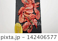 Pink shrimps lie on a black slate board surrounded by lemon slices and a bowl of spices, with a smooth movement of the camera from above to the side. The concept of seafood, cooking, seasoning. High 142406577
