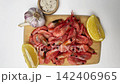 There are pink shrimps on a wooden board, surrounded by lemon slices, garlic and spices on a white background, smoothly approaching from above. Seafood concept, cooking, ingredients. High quality 4k 142406965