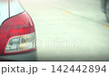 Video 4K rear side of silver car cloeup on tail light. Showing a stationary car parked on the roadside while other vehicles drive past it in urban traffic during daytime. 142442894