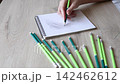 POV hand drawing with pencil in sketchbook on wooden table, artist hatching graphite sketch in spiral notepad with green pencils around, art therapy process, close up 142462612