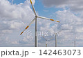 Close-up aerial view wind turbines rotate above harvested farmland beneath dramatic summer clouds. Renewable energy generation wind power infrastructure agriculture sustainability and rural landscape 142463073
