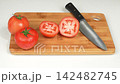 Fresh red ripe tomatoes whole and cut halves with kitchen knife on wooden cutting board, culinary cooking preparation 142482745