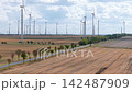 Aerial video shows wind turbines across harvested farmland beside rural road and power lines. Renewable energy landscape combines agriculture, infrastructure and sustainable electricity generation 142487909