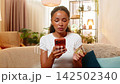 African American young woman on home sofa blocks bank card using smartphone after bank fraud alert 142502340