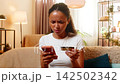 African American young woman on home sofa reviews bank card payments using smartphone banking app 142502342