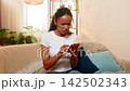 African American young woman on home sofa shocked by unknown bank transaction on smartphone screen 142502343
