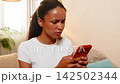 African American young woman on home sofa reading bank alert about unknown card transaction notice 142502344