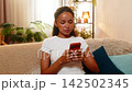 African American young woman on home sofa calmly using phone for mobile online banking with card 142502345