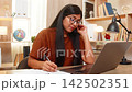 Indian woman on home table listens to client on headset and writes notes during support service call 142502351