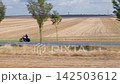 Motorcyclist cruises along rural road beside harvested fields under cloudy sky. Motion blur, travel, freedom, speed, and countryside scenery create dynamic transport scene in open landscape 142503612