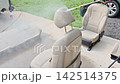 Man uses pressure washer to clean car seat in driveway water sprays onto fabric. 142514375