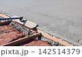 Masonry worker works on concrete slab using trowel at abuilding site is uneven with stones around. 142514379