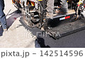 Several workers use tools to spread asphalt on road while paving machines operate nearby. 142514596