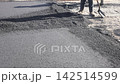 Workers use shovels to spread asphalt on new road in an urban setting 142514599