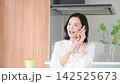 A woman who appears to be a housewife in her 50s, smiling, is using her smartphone at home to talk to family and friends in between household chores. 142525673