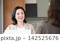 A middle-aged woman smiling and consulting with a client face-to-face; a businesswoman giving explanations and proposals in the office; communication. 142525676