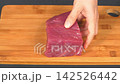 Closeup shot of woman hand slicing fresh raw beef tenderloin steak with sharp knife on wooden cutting board, home cooking culinary preparation 142526442