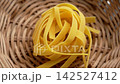 Raw Italian fettuccine pasta nest in braided rattan bowl close up. Uncooked organic healthy natural ingredient. Top View. Rotation 142527412