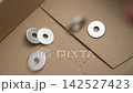 Metallic fastener washers falling into a cardboard box in slow motion. Packaging and delivery of spare parts concept 142527423