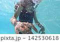 Slow motion view of young girl swimming underwater wearing goggles and waving with her hands 142530618