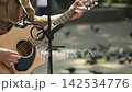 A close-up shot of a young artist playing an acoustic guitar, his hand plucking the strings with a pick, a microphone stand in front of him, slow motion 142534776