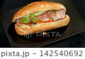 Traditional Vietnamese banh mi pork sandwich slowly rotating on black ceramic plate, crispy baguette street food delicacy 142540692