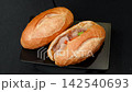 Traditional Vietnamese banh mi pork sandwich next to crispy plain baguette bread rotating on black plate, street food delicacy 142540693