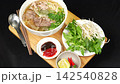 Rotating Vietnamese beef pho noodle soup combo set with fresh herbs and dipping sauce on wooden tray 142540828