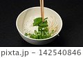 Adding fresh bean sprouts and green herbs into rice noodle bowl with wooden chopsticks, Vietnamese pho cooking preparation 142540846